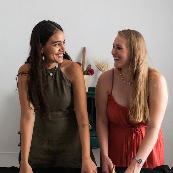 Two people smiling and supporting each other in a yoga studio.